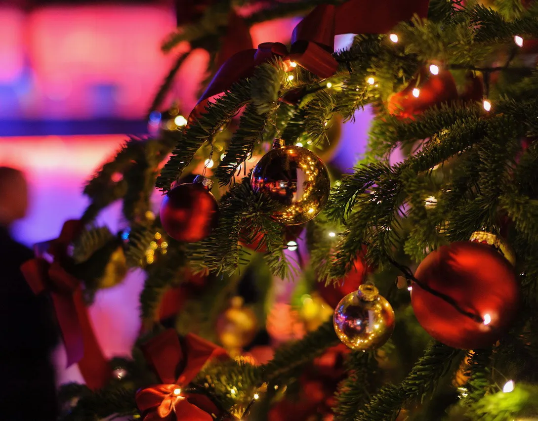 Christmas tree with red and gold baubles and fairy lights, a blurred guest in pink light behind it